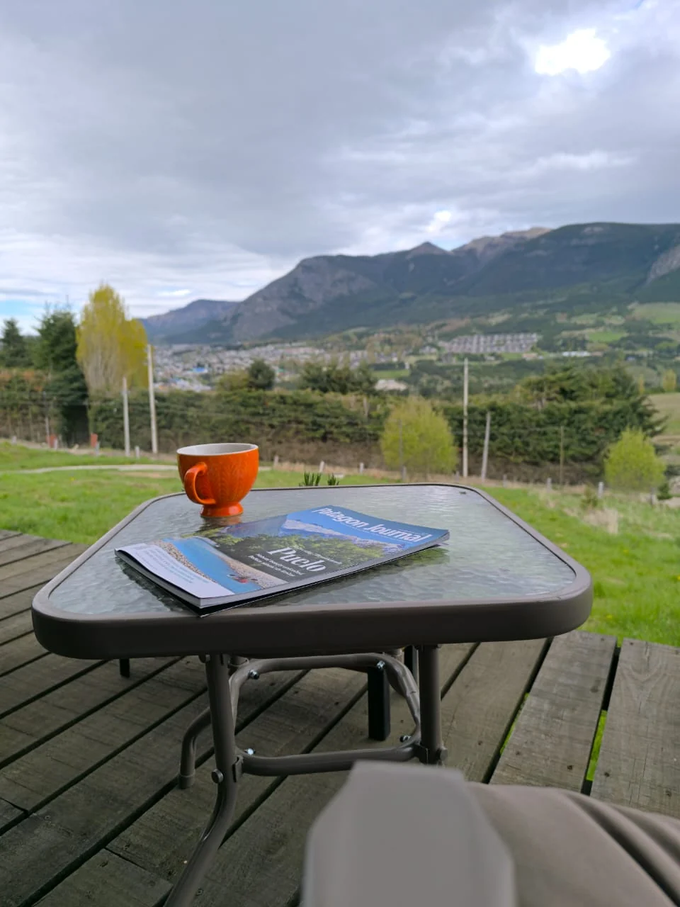 Taza de café y revista sobre la mesa de la terraza, con vista a los cerros de Coyhaique