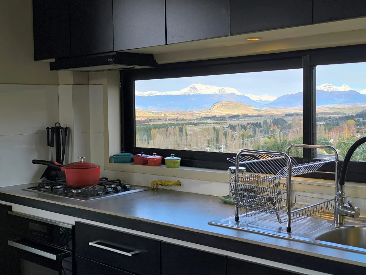 Cocina con ollas rojas y lavaplatos frente a un ventanal con vista a la cordillera nevada