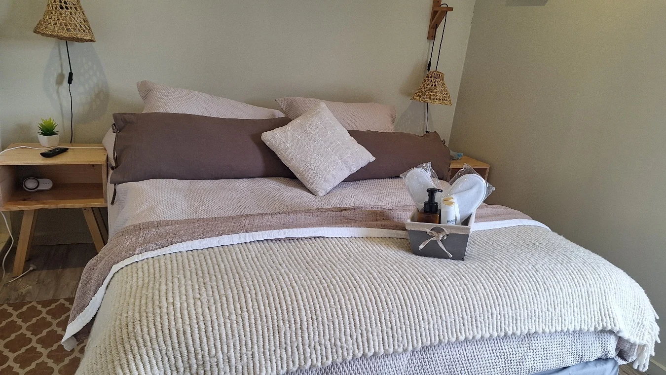 Cama matrimonial con manta tejida, cojines y lámparas de mimbre en el dormitorio principal